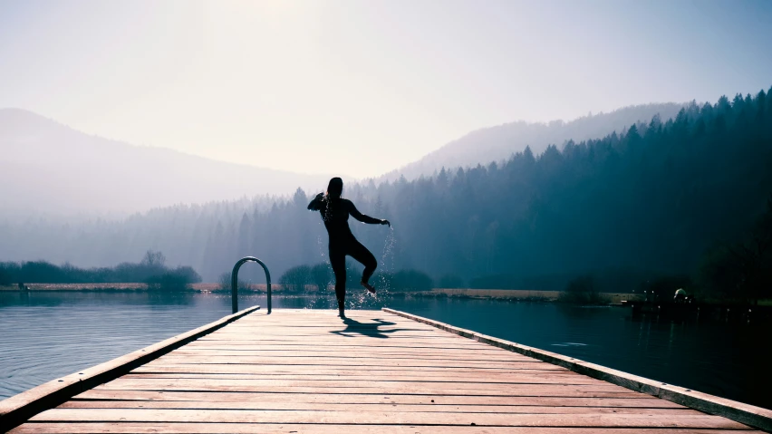 a woman walking on a pier with the sun setting in the background