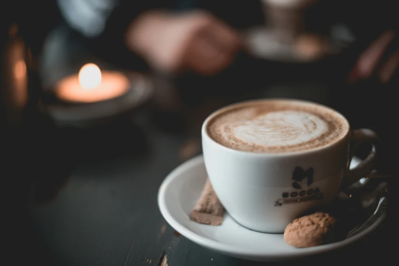 a cappuccino sits on a plate and with a lit candle in the background