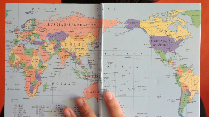 a person holding an open book showing a map of the world