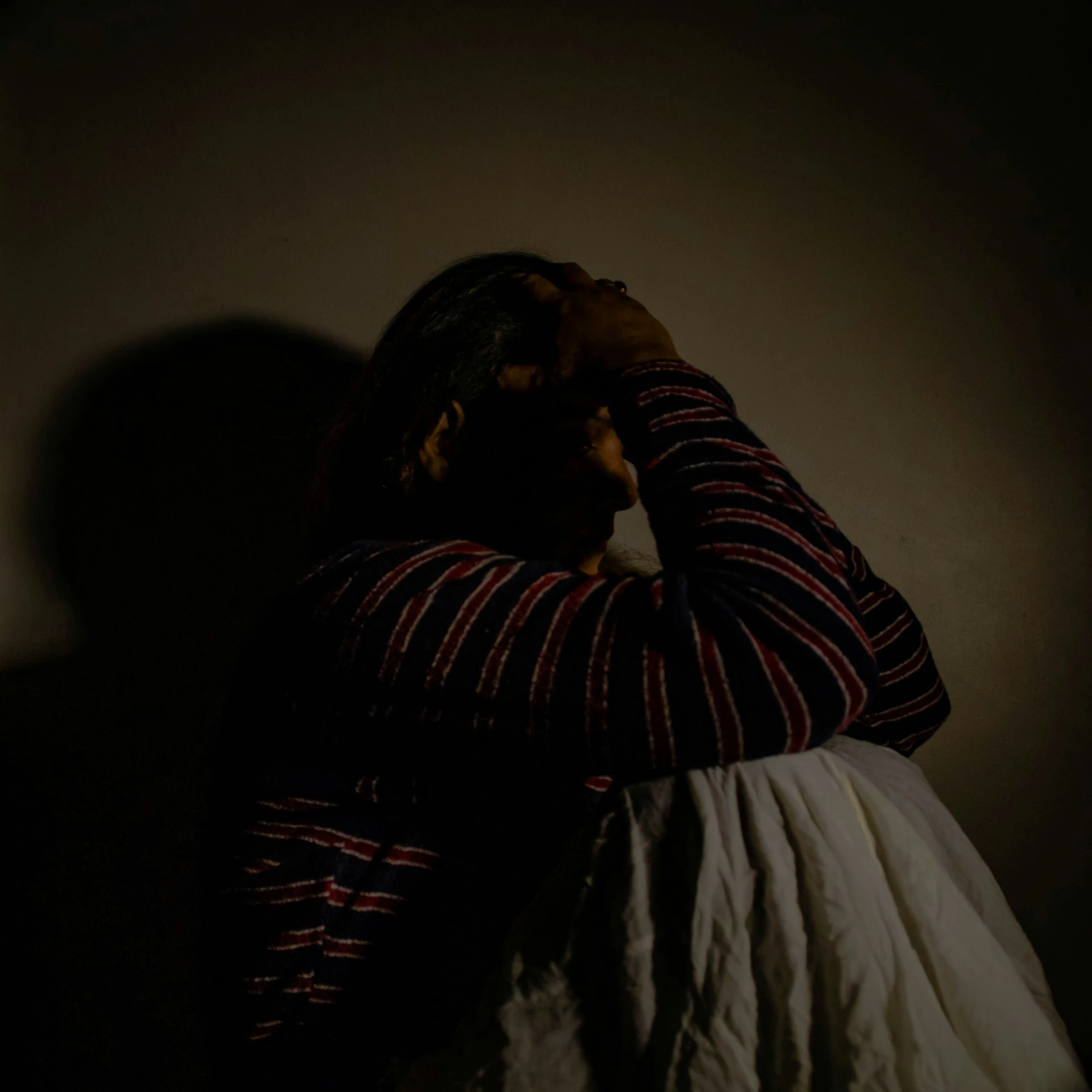 a dark portrait of a person sitting down and holding their head in their hands