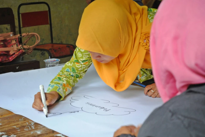 two young women, one writing in front of her drawing