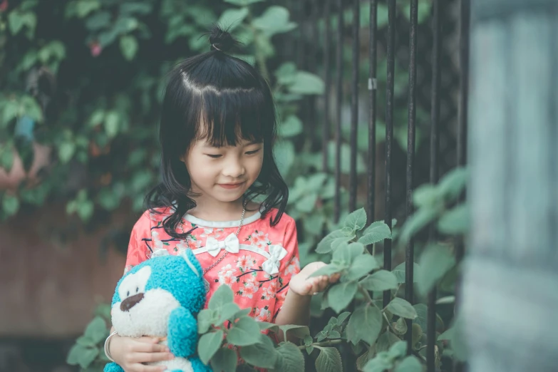 a child holding a teddy bear near a fence