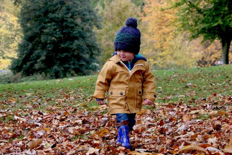 a child wearing a winter hat and boots walking on dry leaves