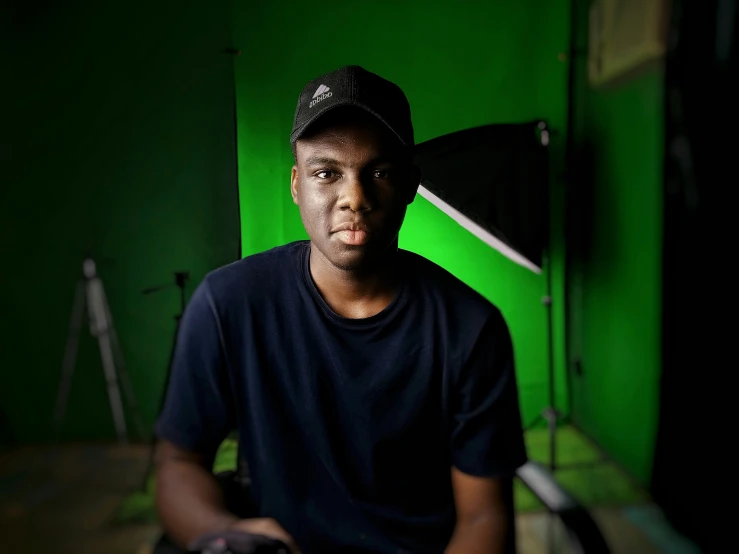 a man with a hat on, sitting in front of a green wall