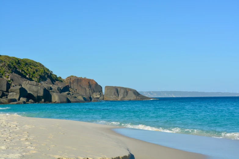 a sandy beach with a large rock outcropping the shore