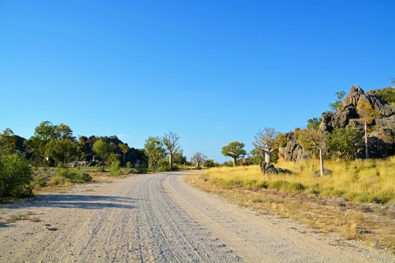 a gravel road has no trees on the side and a hill in the distance