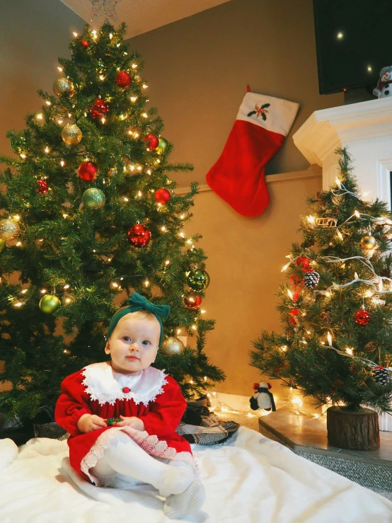 a baby wearing a elf outfit sitting on the floor in front of a christmas tree