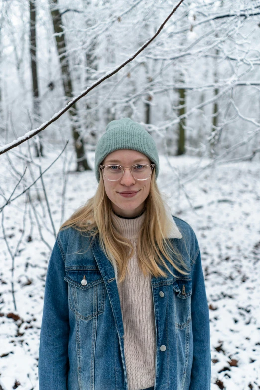 a woman in glasses and a denim jacket standing in the snow