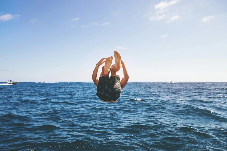 person jumping into the water while another boat sails by