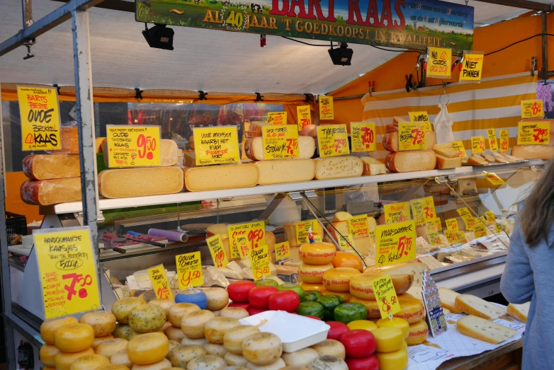 people at a market stand selling cheeses and other foods