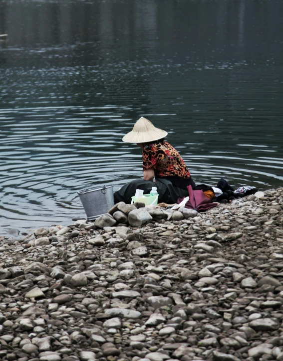 there is a woman sitting on the rocks by the water