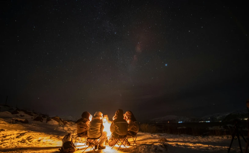 three people sitting around a campfire at night