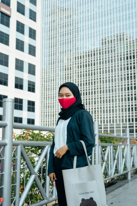 a young lady walking down a sidewalk carrying a bag with her face covered by a mask