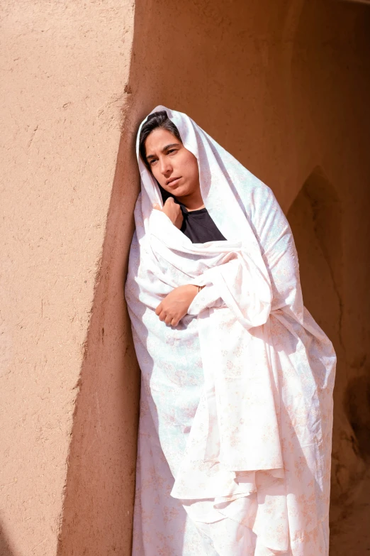 a women wearing a white blanket leaning against a wall