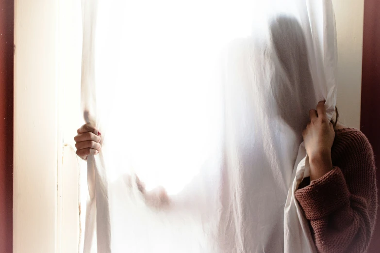 a woman peeking through a window while the curtains d her