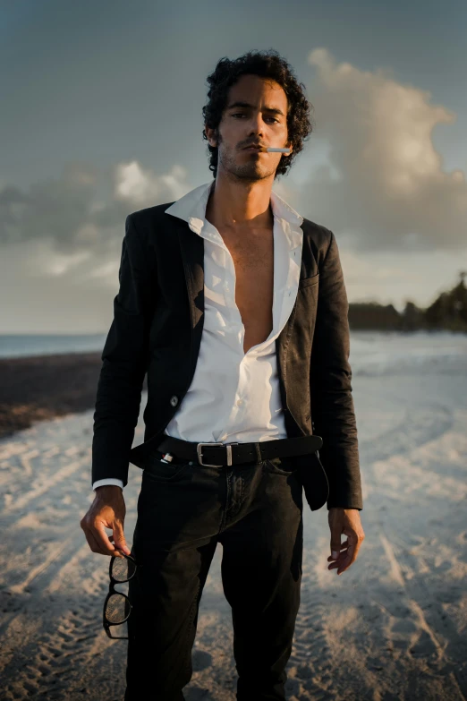 a man with a beard and black jacket is standing on the beach