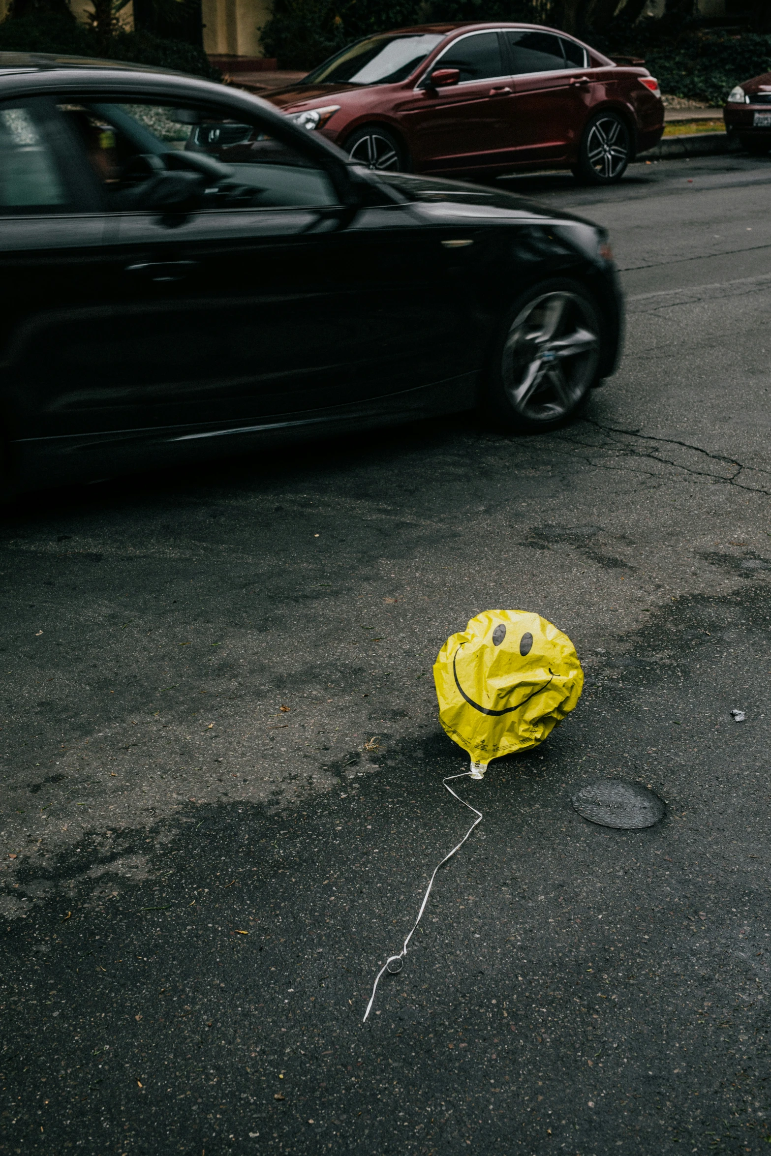 a yellow smiley face sitting on the street by a black car