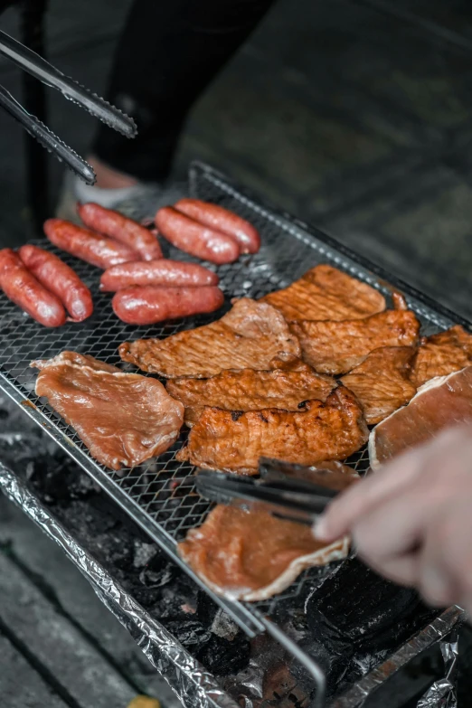 a person is grilling some meat and sausages