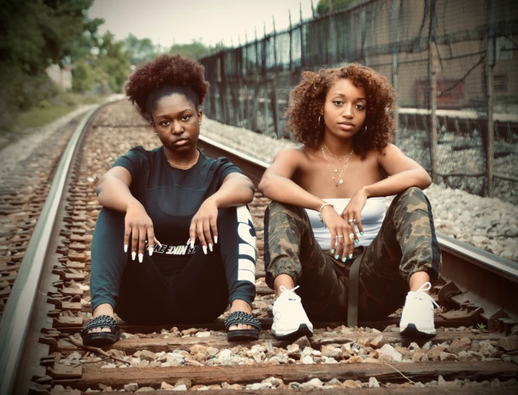 two african girls on railroad tracks leaning out of their shoes