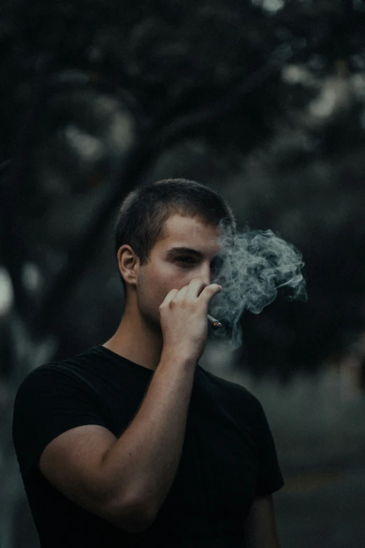 a young man smokes on a cigarette as the light illuminates him