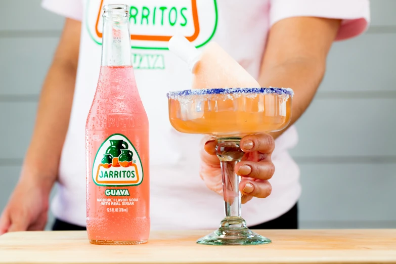 person wearing a white shirt holding up a pink drink next to it