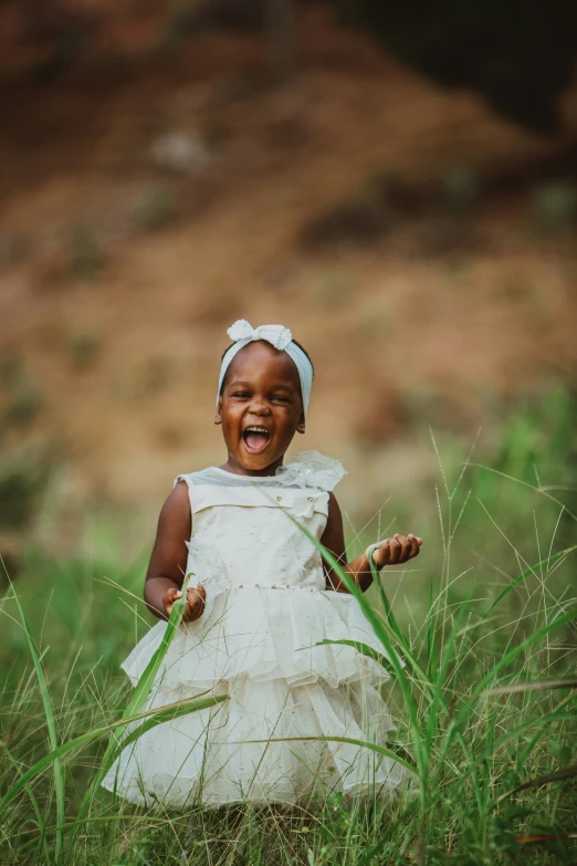 a baby in white sitting in grass laughing at the camera