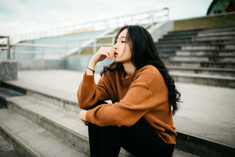 a woman in brown sweater sitting on steps looking off to the side