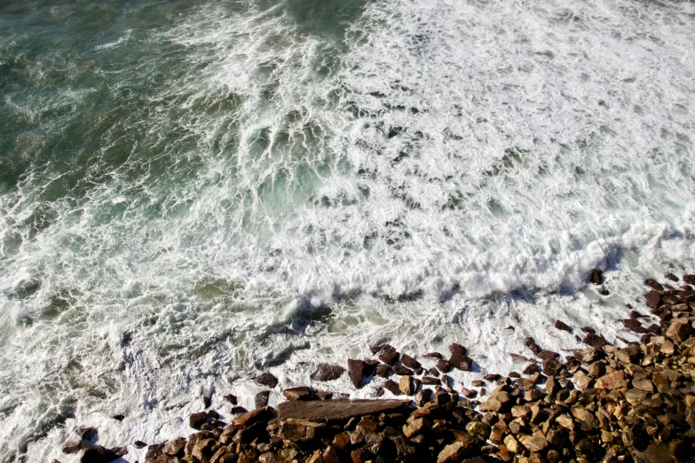 a view from above looking down at an ocean with rocks and pebbles