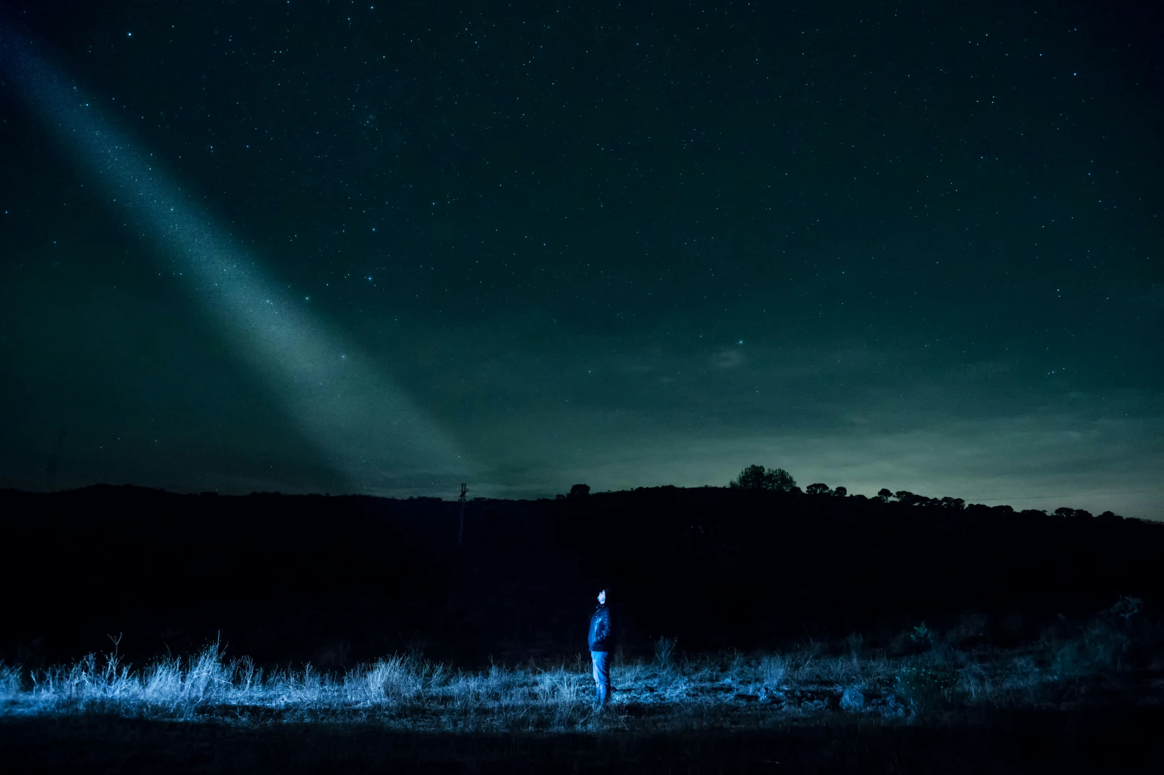 a dark night sky and a person standing in a field with a light beam