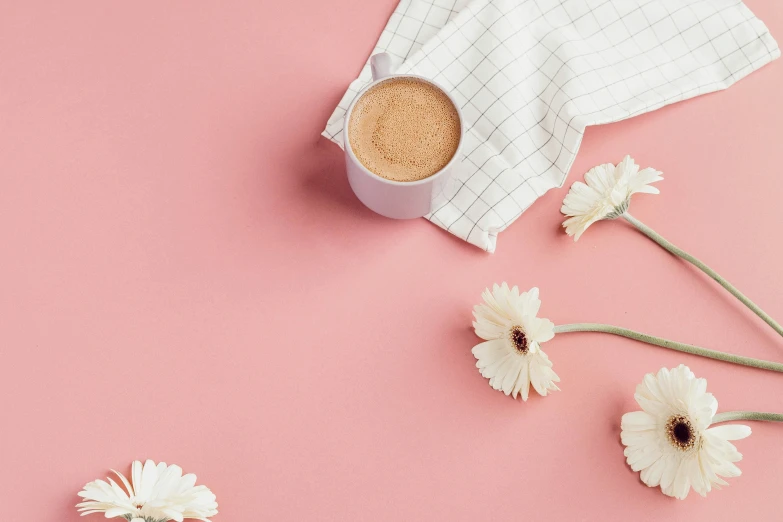 white flowers and a cup of coffee sitting on a pink background