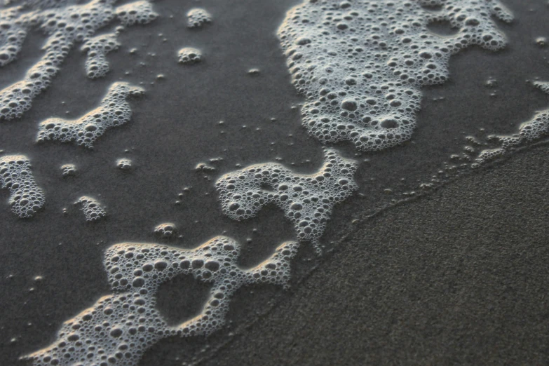 a very close up po of white foam on black sand