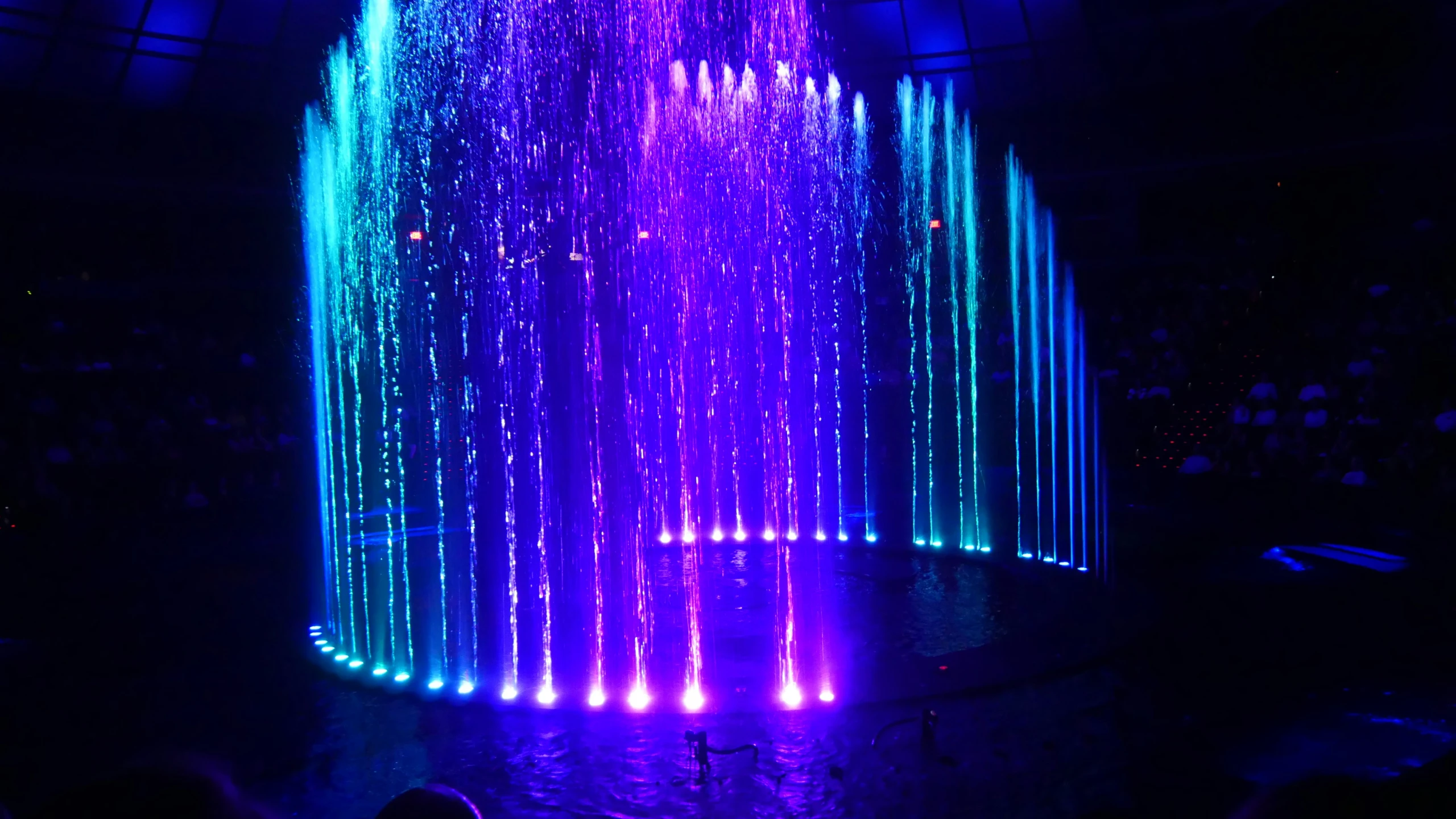 a multicolored water fountain has lights and is lit in the dark