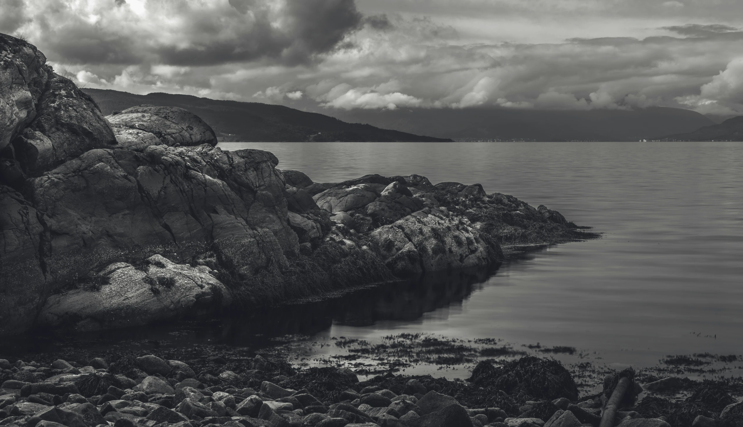 a black and white po of water, rocks, and clouds