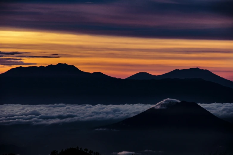 a sunrise over mountains with clouds below