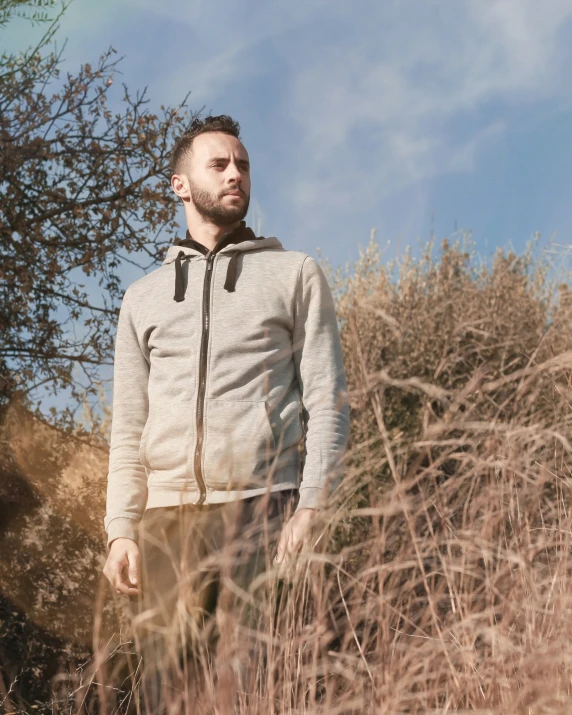 a bearded man stands in an overgrown field