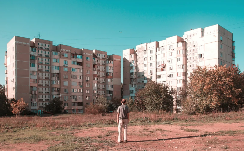 a man standing on the edge of a field in front of some tall buildings