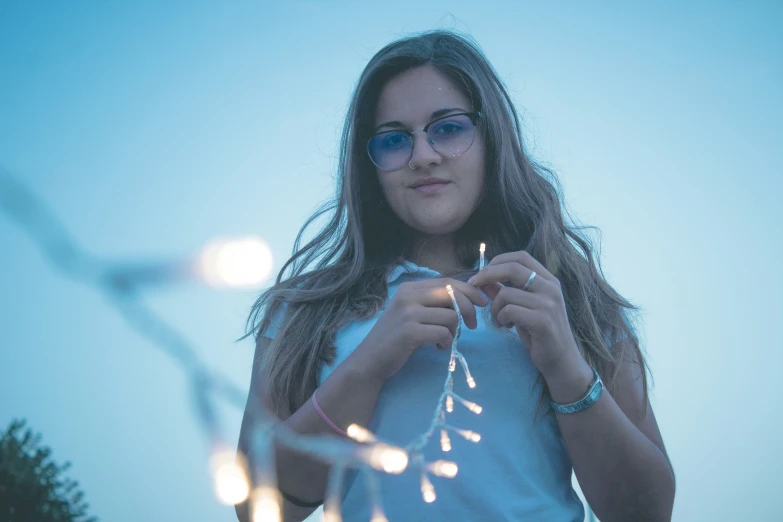 a beautiful young lady holding up some string lights