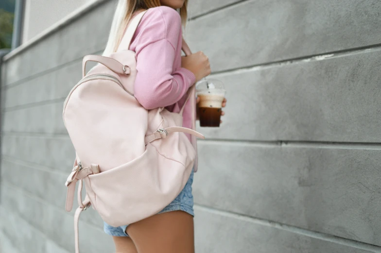 a woman wearing short shorts holding a backpack and drinking coffee