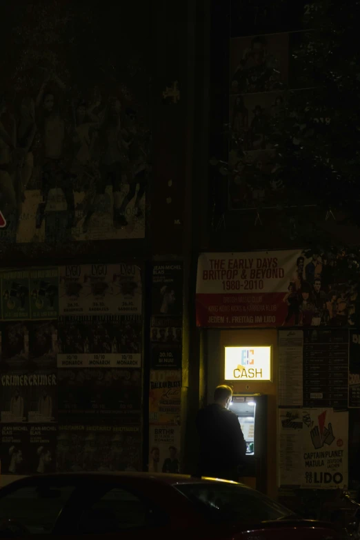 an illuminated payphone stands next to a wall of advertits