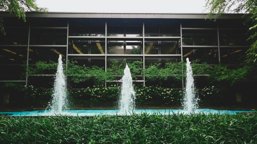 four fountains spouts in front of a glass walled wall