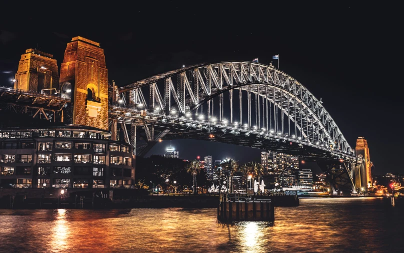 the sydney bridge is illuminated at night, and the buildings can be seen in the background