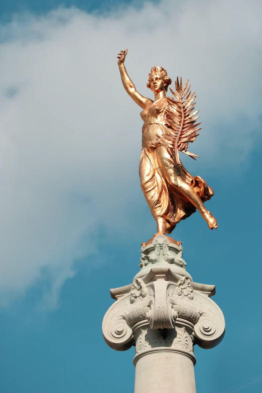 the statue is gold colored and is located atop a pole