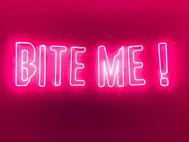 the word bite me painted on a neon pink wall