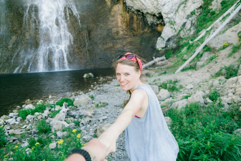 a woman standing near a waterfall holding her hand