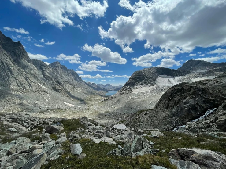 a rocky area with grass and rocks, mountains and clouds