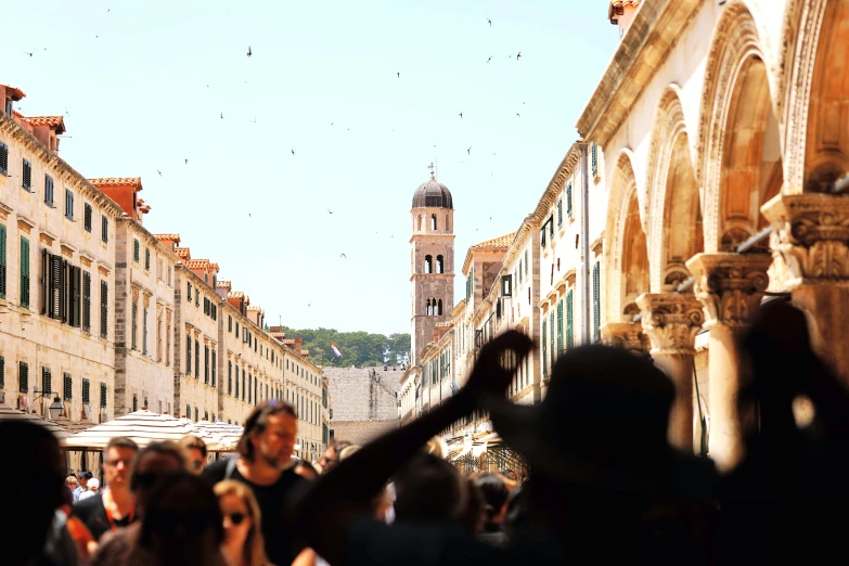 an upward view of several people in front of buildings and a clock tower