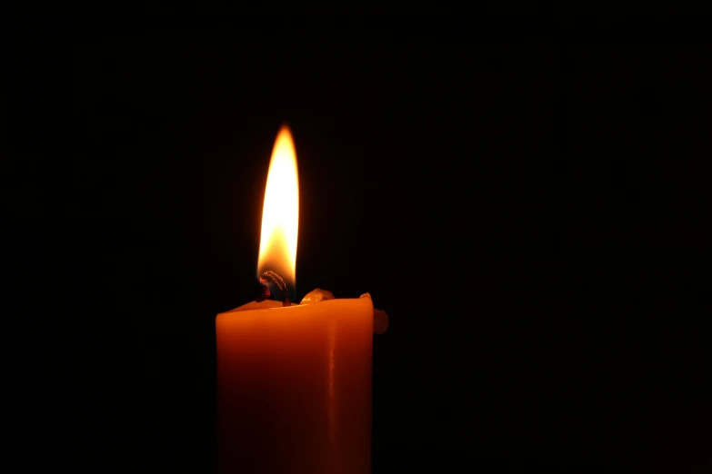 a single lit candle in the dark with its light shining