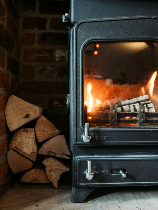 a wood burning in an outdoor oven with firewood nearby