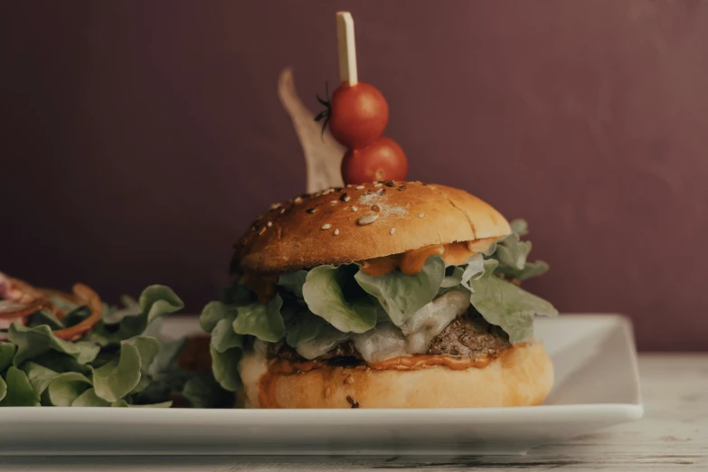 a hamburger is sitting on a white plate and being served with greens and a cherry tomato on top