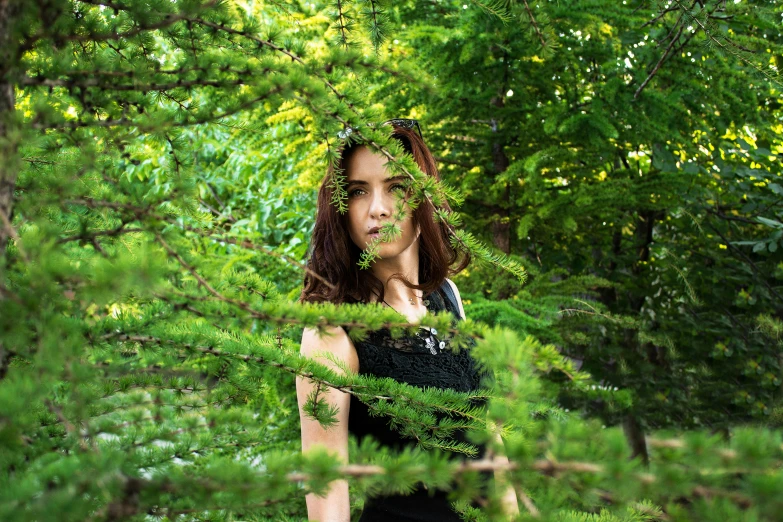 a woman hiding behind a green bush in the forest